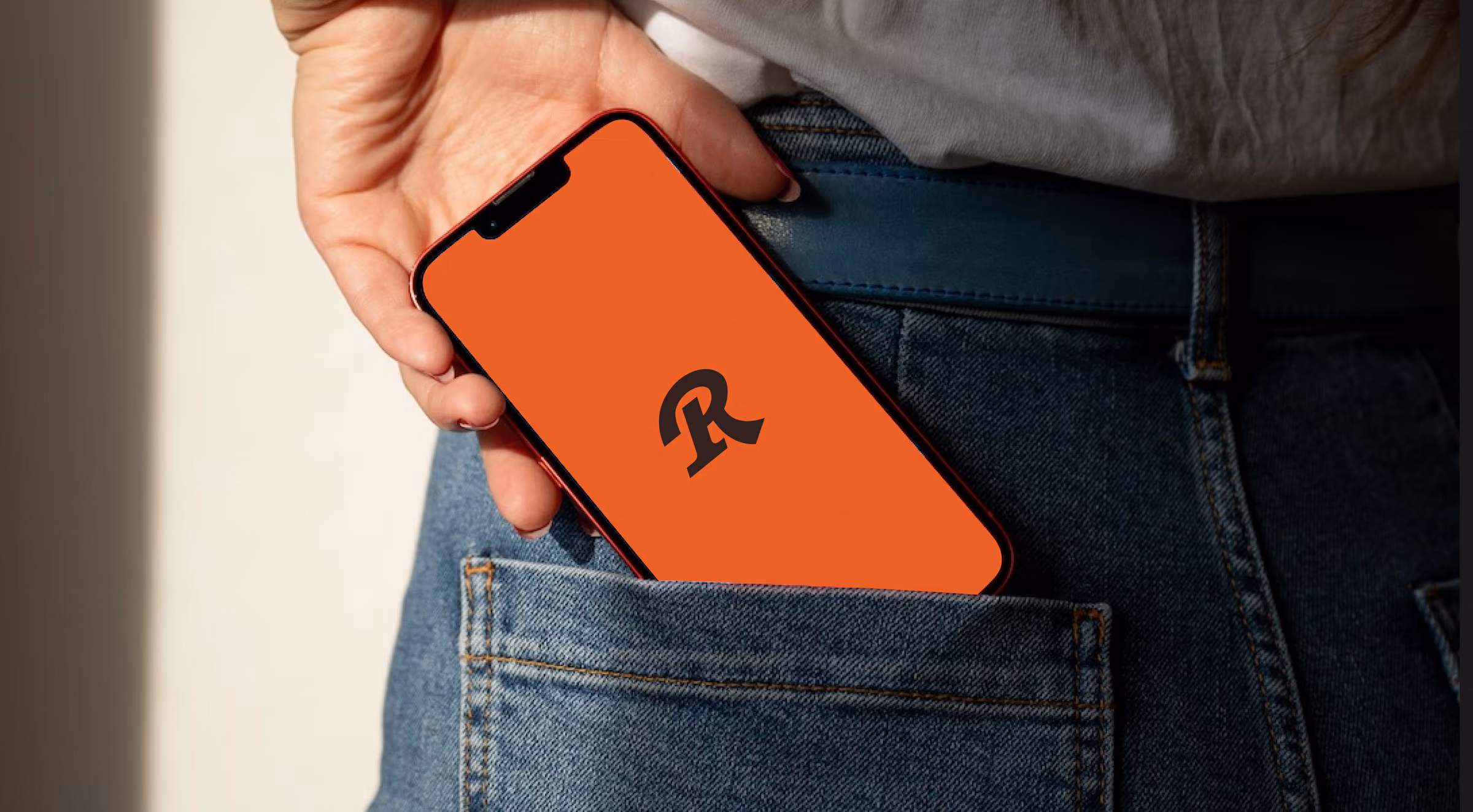 Hand slipping a phone showing the Remono R monogram into a jeans pocket