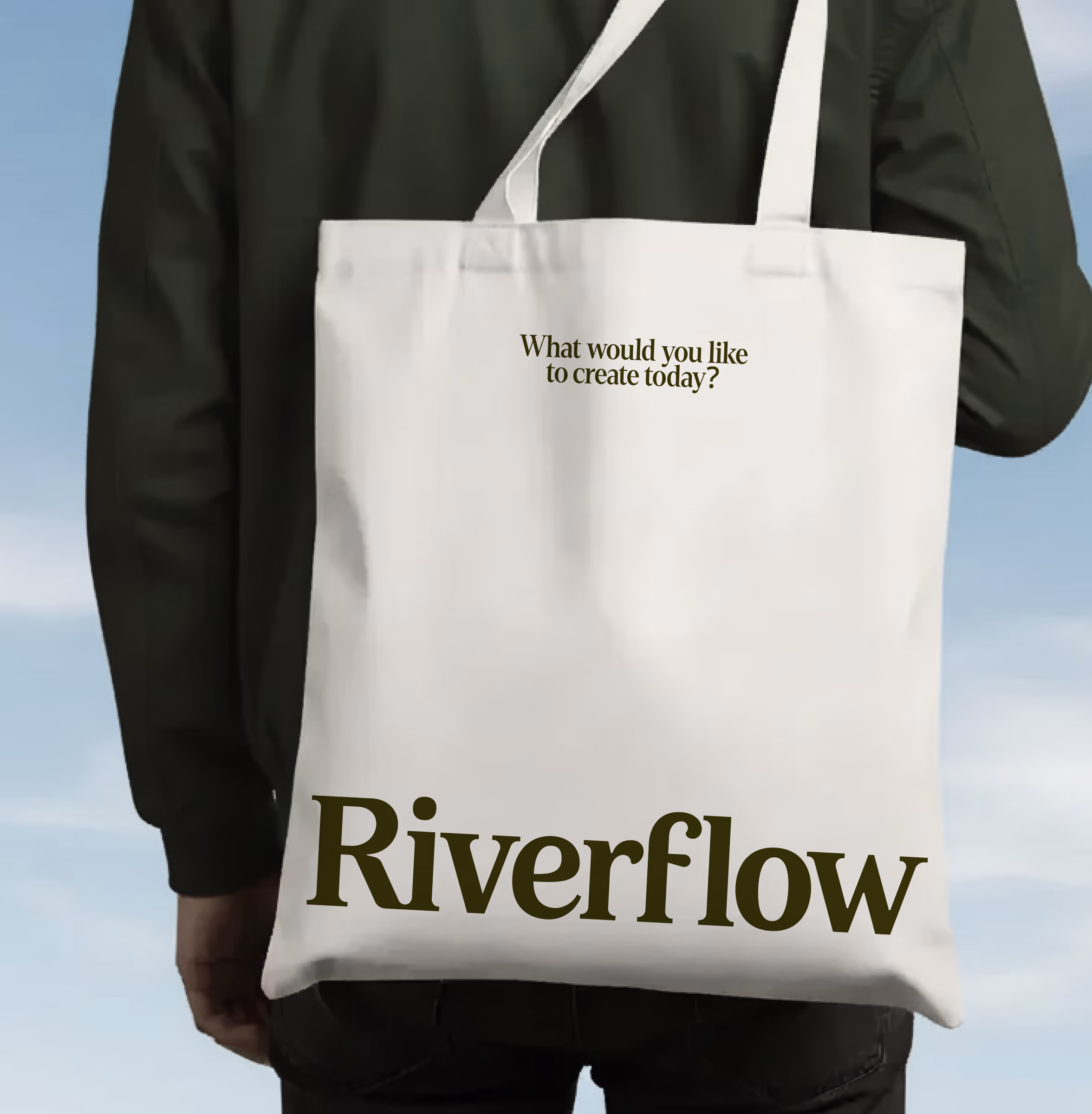 Riverflow tote bag printed with 'What would you like to create today?' and the wordmark, carried over a shoulder
