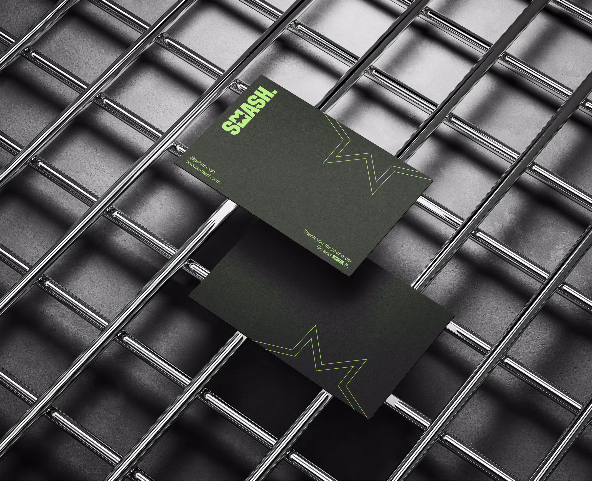 Dark green Smeash business cards with green wordmark and star outline, laid on a metal grid