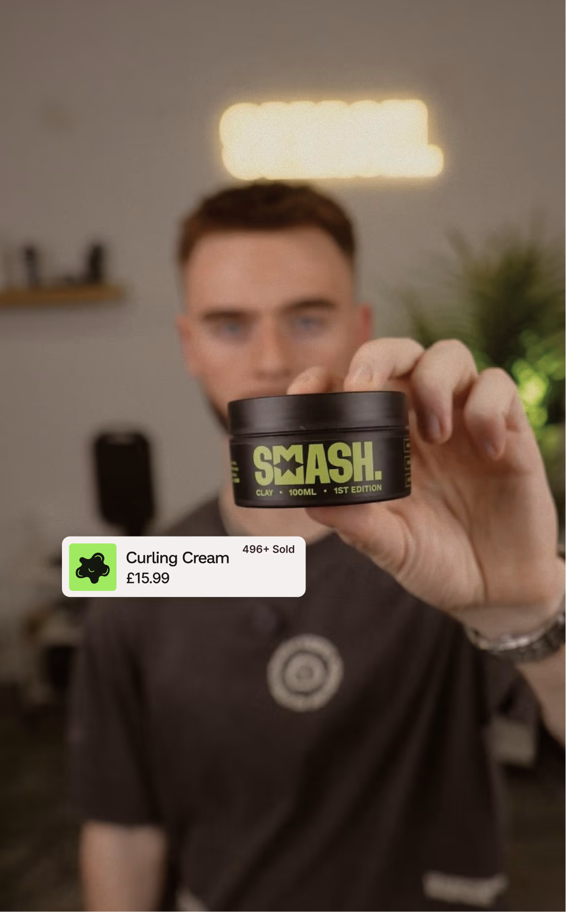 Man in a barbershop holding a Smeash clay tin, with a shop tag for curling cream at 15.99